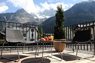A bottle of champagne sits on a balcony with mountains in the background