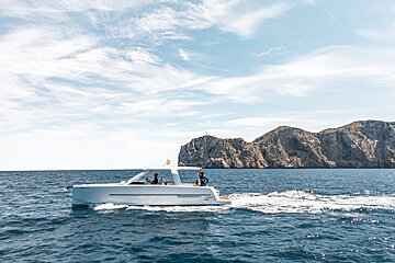 A white boat is floating in the ocean with mountains in the background