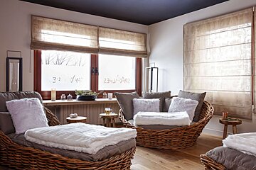 A cozy spa relaxation room with wicker chaises, plush white blankets, and large frosted windows displaying