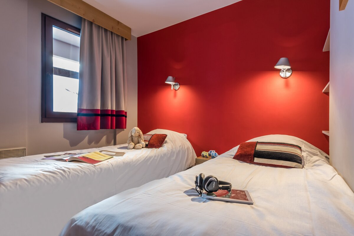 A bedroom with two beds and a red wall
