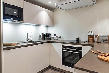 A modern, well-lit kitchen featuring light cabinets, dark countertops, built-in oven and microwave, a sink, stovetop, toaster, and various appliances.
