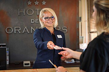 A woman giving a credit card to another woman in front of a sign that says hotel de oranges