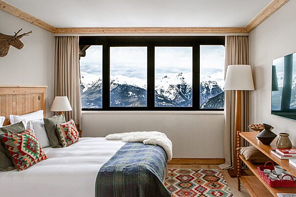 A bedroom with a bed and a window with mountains in the background
