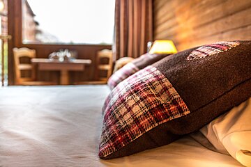 A plaid pillow with a heart on it sits on a bed