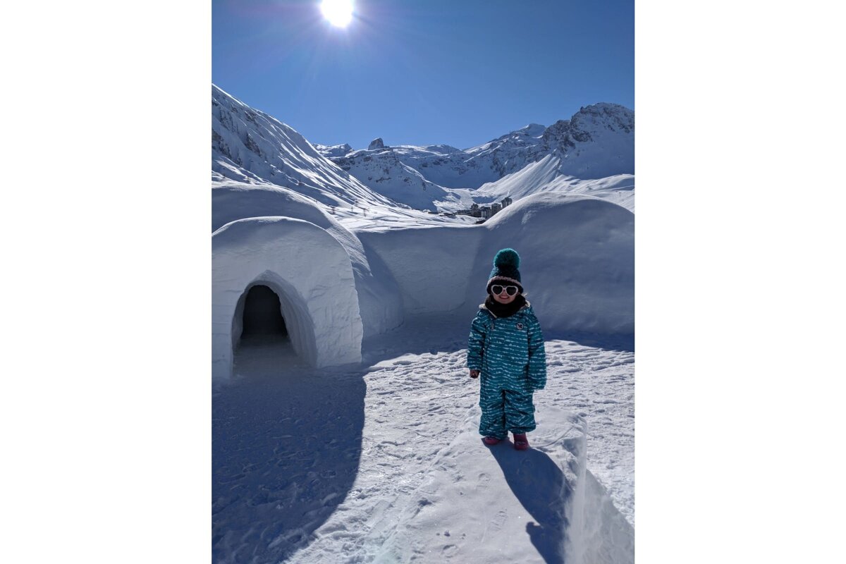 A little girl standing in front of an igloo in the snow