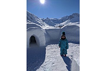 A little girl standing in front of an igloo in the snow