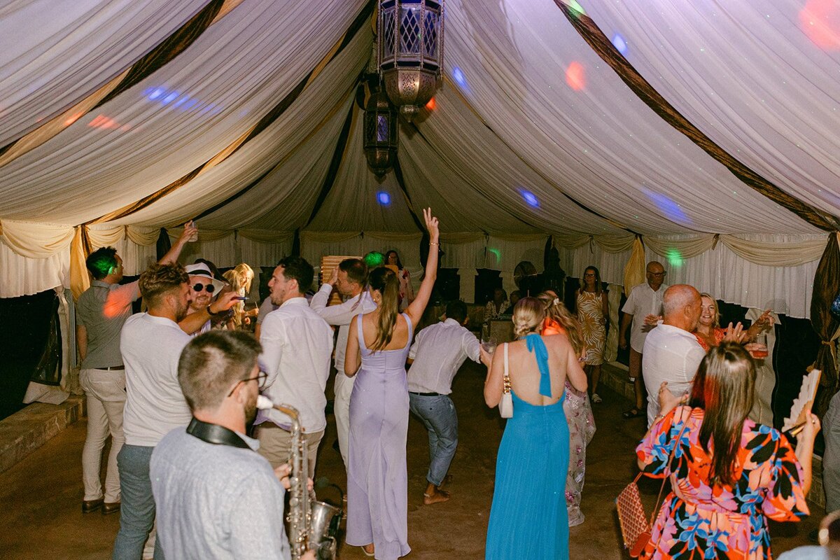 A group of people are dancing under a white tent