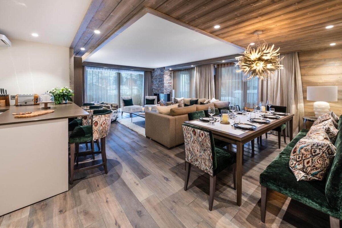 A stylish open-plan living/dining room with a rustic-modern feel. It features a set dining table, kitchen island, comfortable lounge, and wood accents.