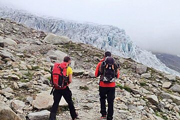 Two men with backpacks are walking down a rocky trail