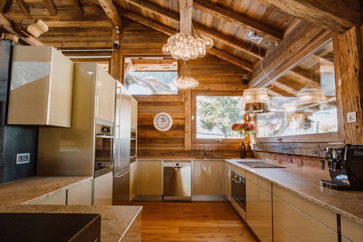 A luxurious, modern kitchen with cream cabinets, stainless steel appliances, and sleek countertops contrasts beautifully with rustic wooden walls, ceiling, and unique bubble chandeliers.