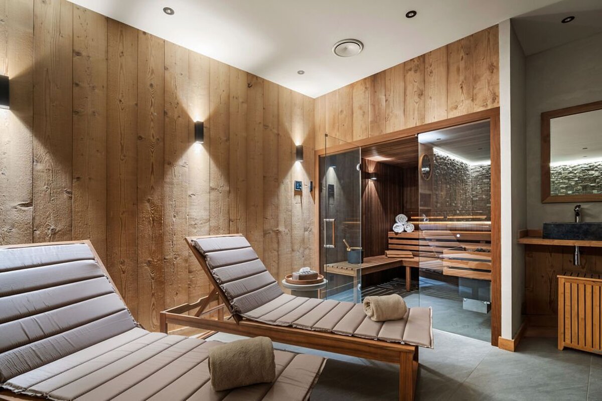 A wooden sauna with a glass door and two lounge chairs