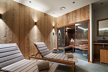 A wooden sauna with a glass door and two lounge chairs
