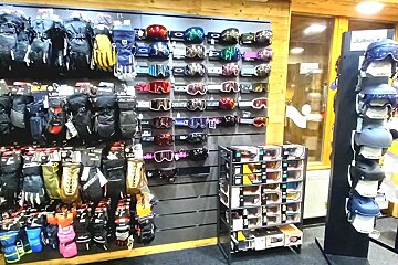 A sports store aisle featuring a diverse collection of ski and snowboard equipment: colorful goggles, numerous gloves and mittens, and helmets.