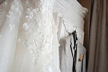 A wedding dress and a tuxedo are hanging on a rack