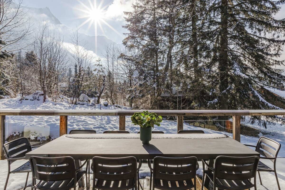 A table and chairs on a snowy deck with mountains in the background
