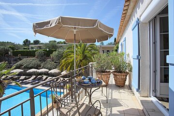 A balcony with a table and umbrella overlooking a swimming pool