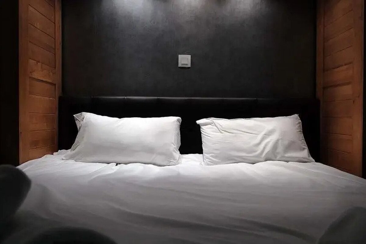 A bed with white sheets and pillows in a dark room