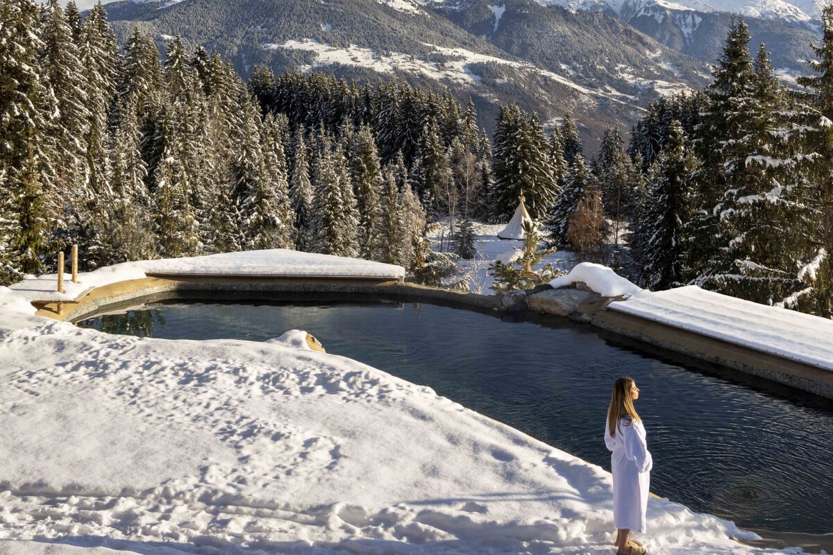 A woman in a bathrobe stands in front of a snow covered pool