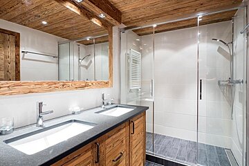 Chic modern bathroom featuring a rustic wooden ceiling, double vanity with dark countertops, and a sleek glass shower.