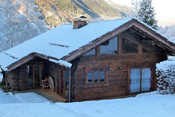 A wooden house covered in snow with mountains in the background