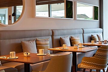 Modern cafe/restaurant with comfortable booth seating, wooden tables, and mirrors with green moss accents. Cups are set on tables.