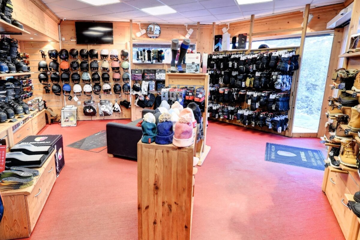 A winter sports gear shop displaying helmets, boots, gloves, and knitted hats. It features wooden walls and a red floor.