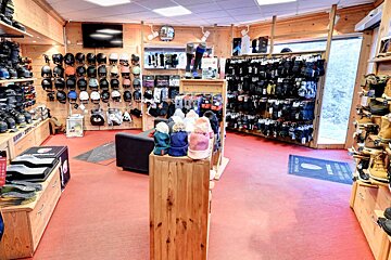 A winter sports gear shop displaying helmets, boots, gloves, and knitted hats. It features wooden walls and a red floor.