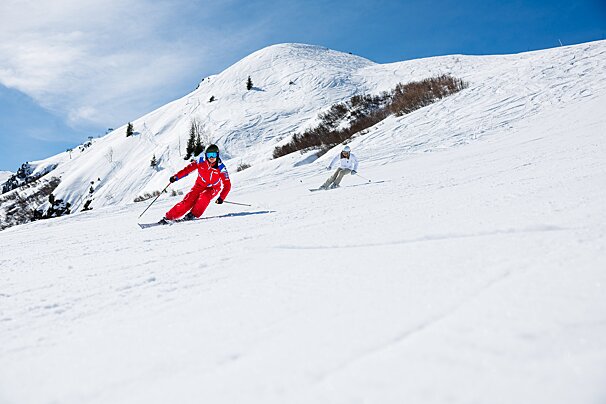 Two people skiing down a snow covered slope with a mountain in the background