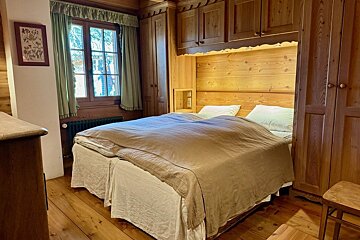 Cozy, wood-paneled bedroom with a double bed, built-in wooden cabinets, and a window with green curtains, creating a rustic feel.