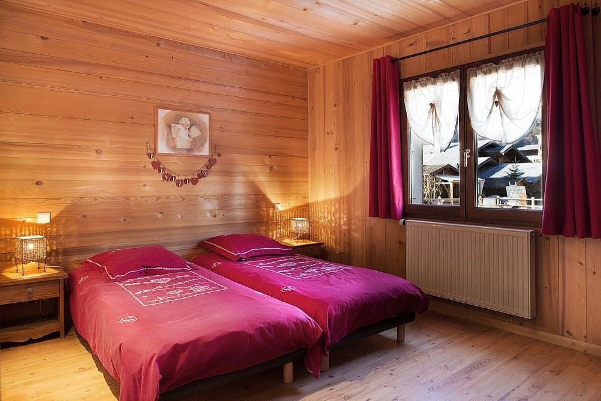 A bedroom with two beds and a window with red curtains