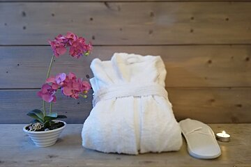 A white robe sits on a table next to a potted plant and a candle