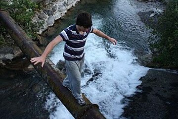 a man walking along a log over a river in morzine