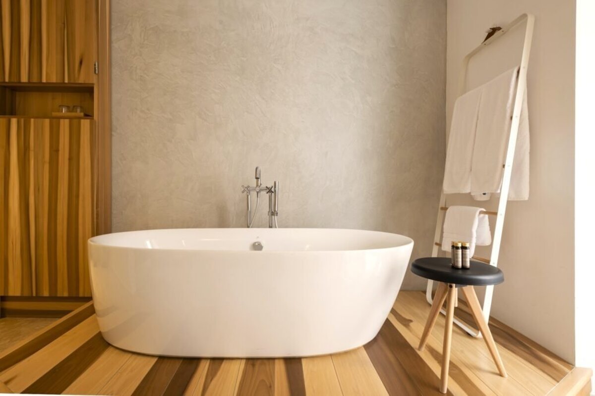 Minimalist bathroom with a white freestanding tub on striped wood flooring, a textured wall, and a white towel ladder.