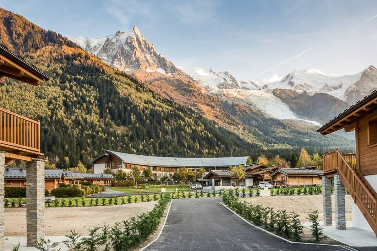 A large building in the middle of a forest with mountains in the background