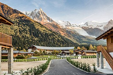 A large building in the middle of a forest with mountains in the background