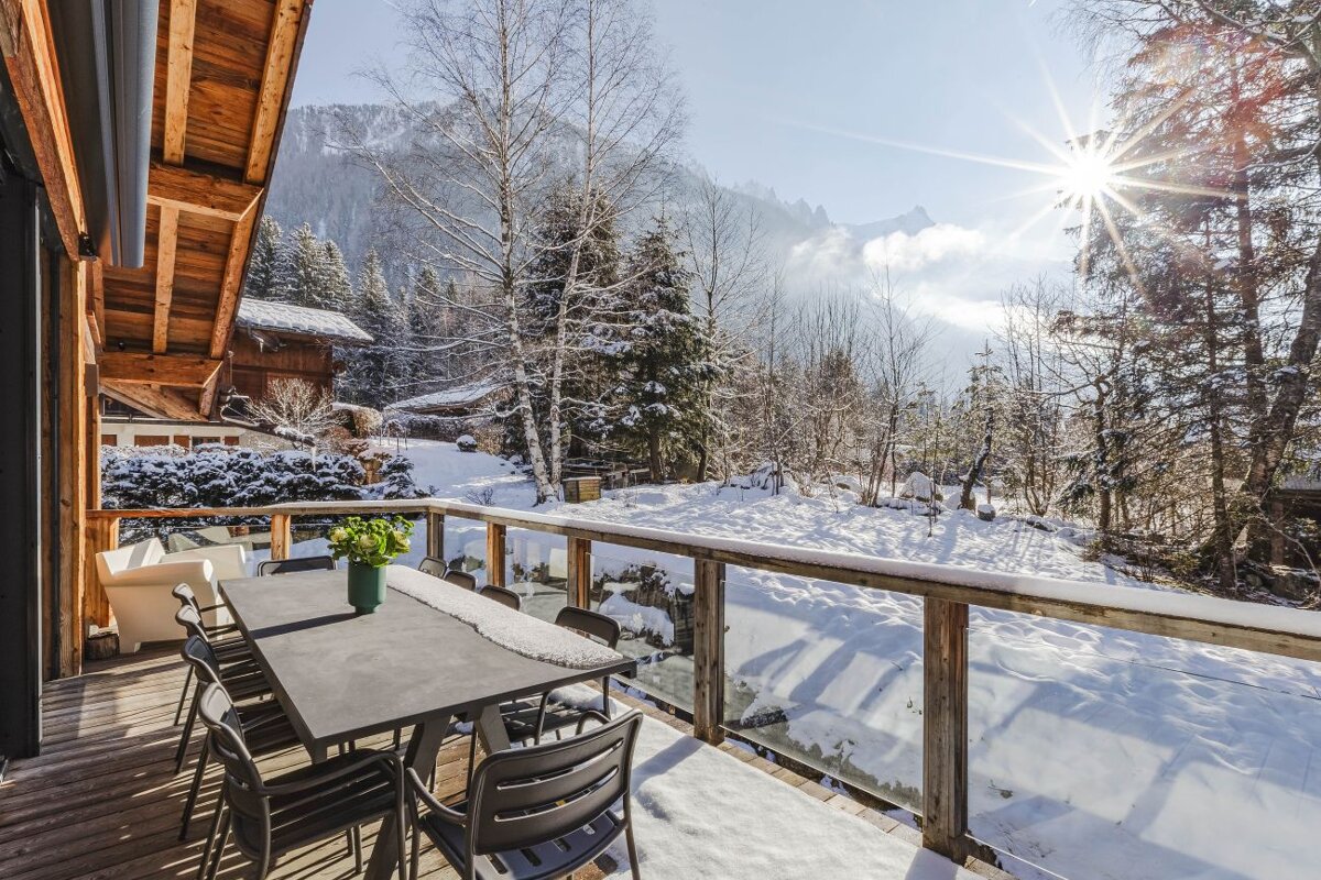 A table and chairs on a snowy deck with mountains in the background