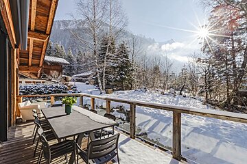 A table and chairs on a snowy deck with mountains in the background