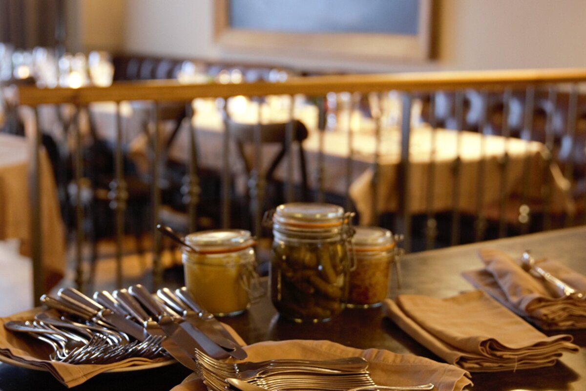 Jars of pickles sit on a table with silverware