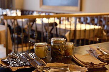 Jars of pickles sit on a table with silverware