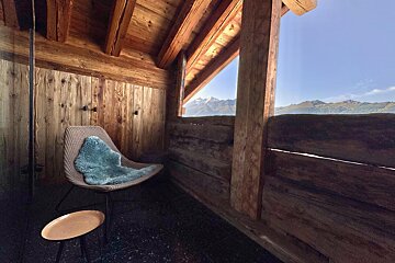 A chair with a blue blanket on it sits on a balcony overlooking the mountains