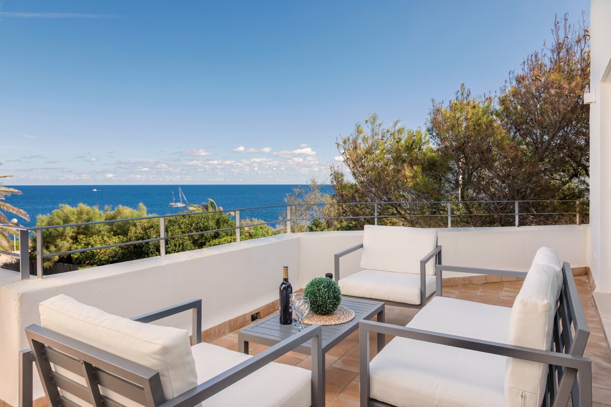 A bottle of wine sits on a table on a balcony overlooking the ocean