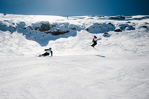 Two people skiing down a snow covered slope on a sunny day