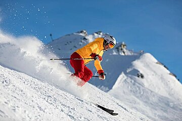 A man in a yellow jacket is skiing down a snow covered slope