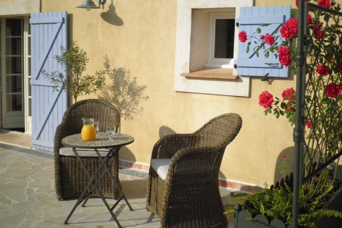 A patio with wicker chairs and a table with a pitcher of orange juice on it