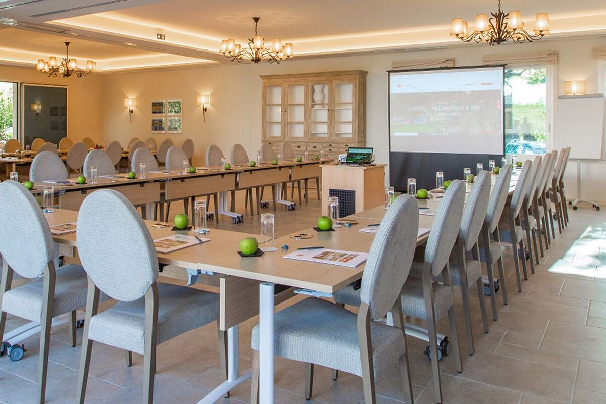 A large conference room with tables and chairs and a projector screen that says hotel bellevue & spa