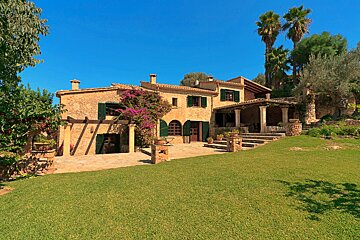 A large stone house with green shutters sits on top of a lush green hillside