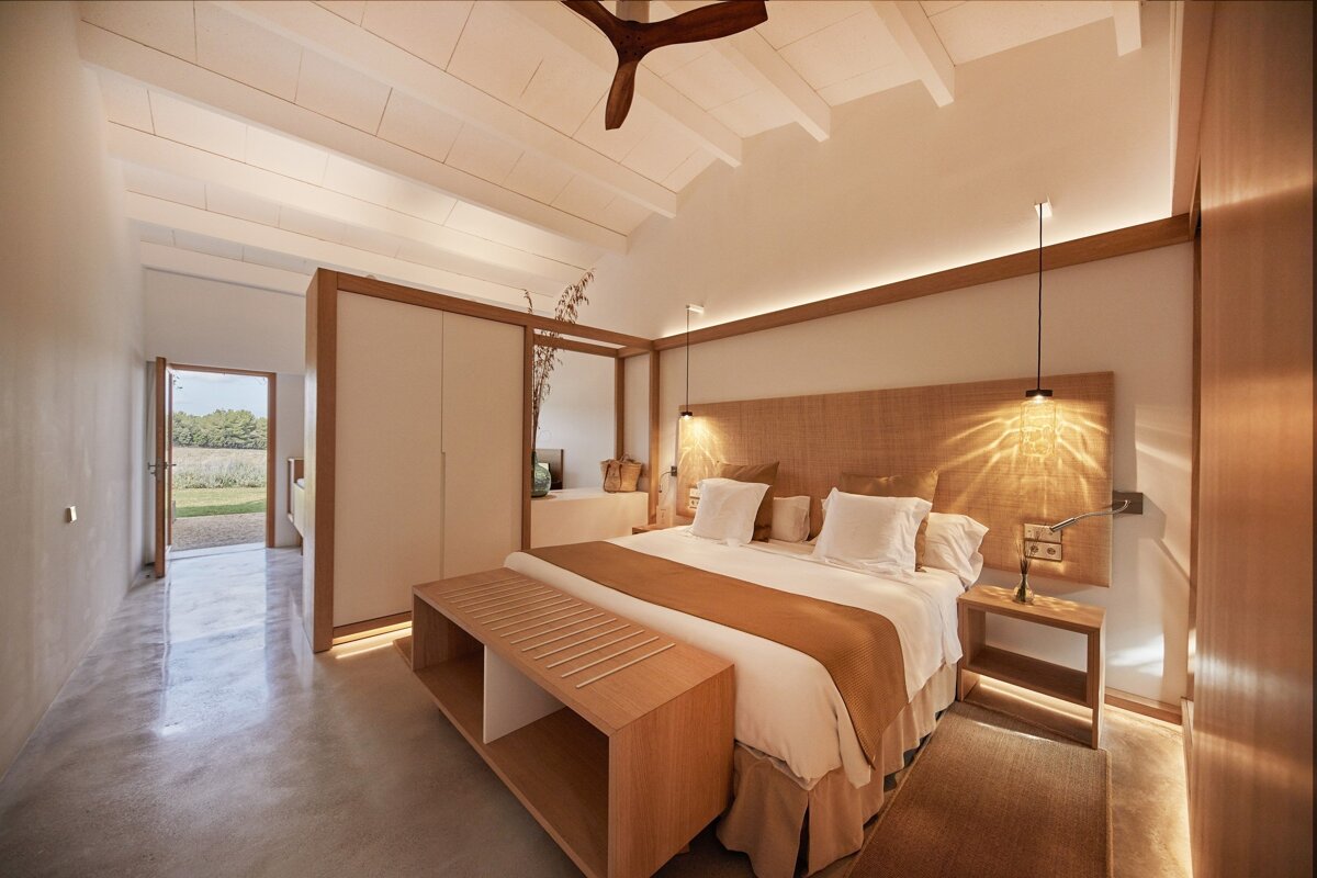 Serene, modern bedroom in natural wood tones with a large bed, vaulted ceiling, and a doorway opening to a peaceful outdoor landscape.
