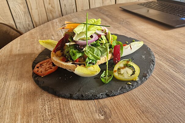 A salad on a plate with a laptop in the background