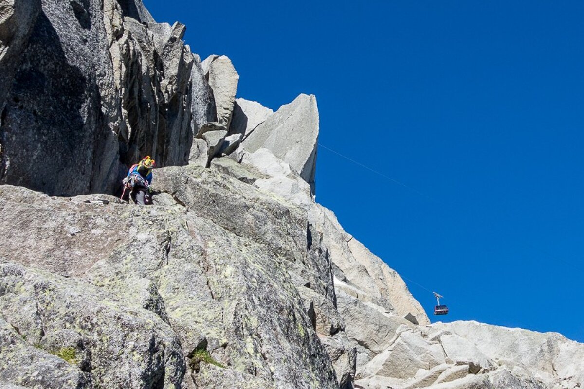 A person climbs a mountain with a cable car in the background