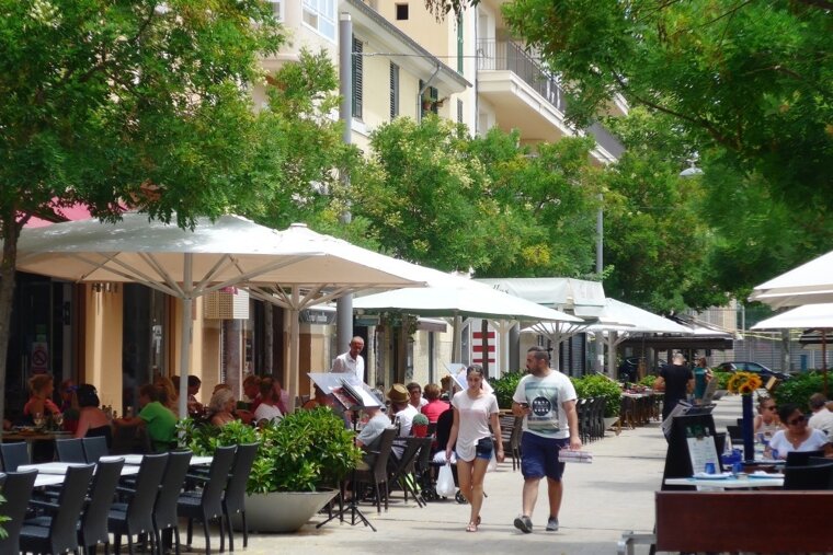 A man wearing a shirt that says ' hawaii ' on it walks down a street